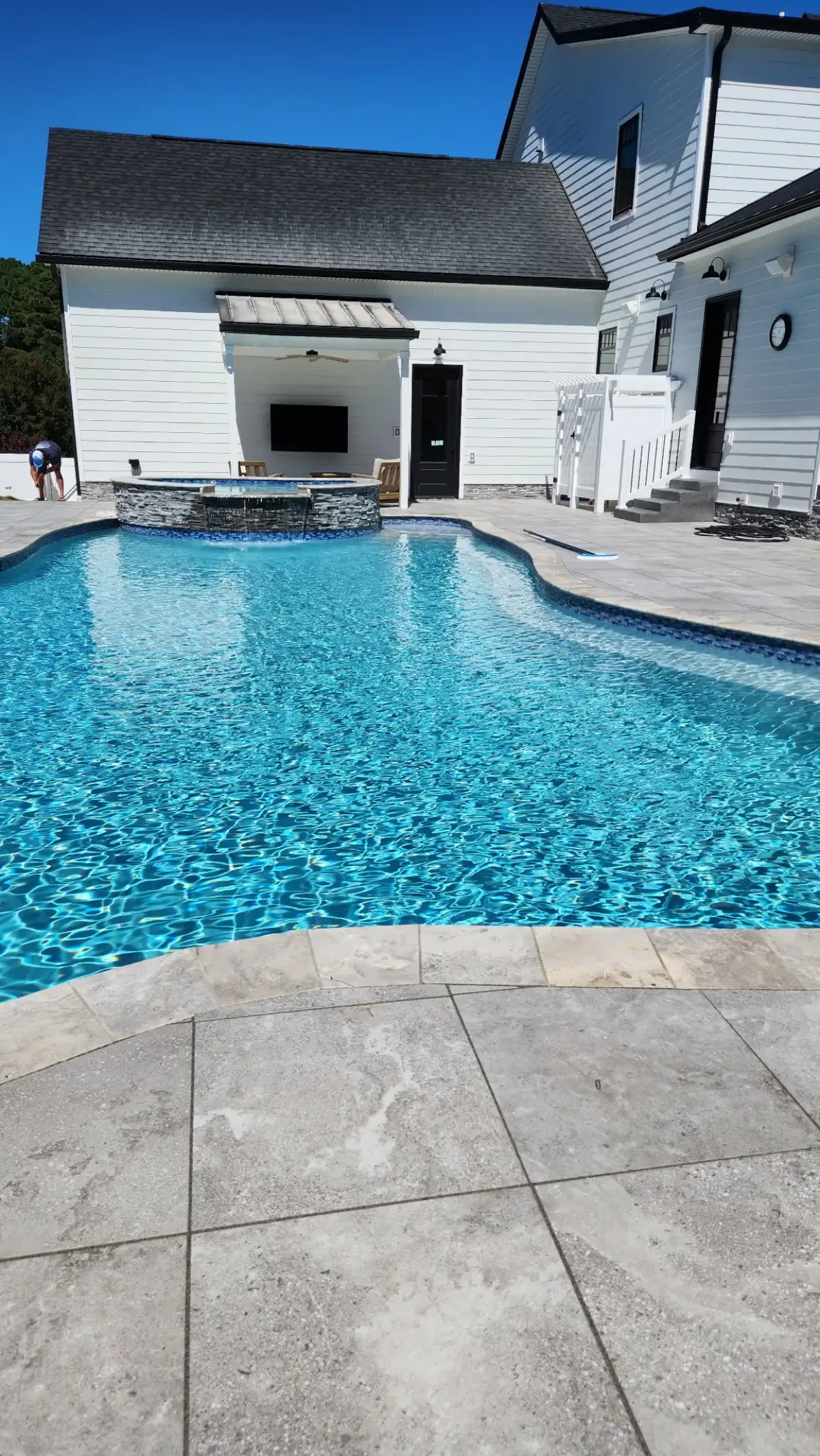 Swimming pool beside a paver deck and white fence